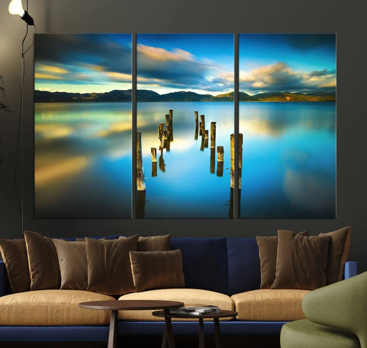 A triptych of a serene lake scene with old wooden pillars, blue sky, and clouds casts a coastal ambiance. The Sea Ocean Sunset Beach Wall Art Canvas Print reflects the soothing nature of the ocean.