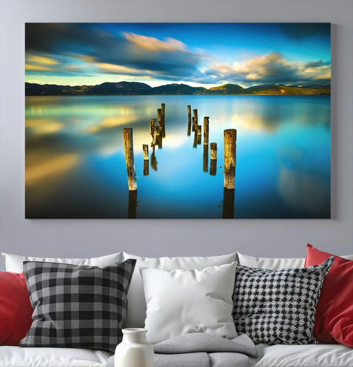 A triptych of a serene lake scene with old wooden pillars, blue sky, and clouds casts a coastal ambiance. The Sea Ocean Sunset Beach Wall Art Canvas Print reflects the soothing nature of the ocean.