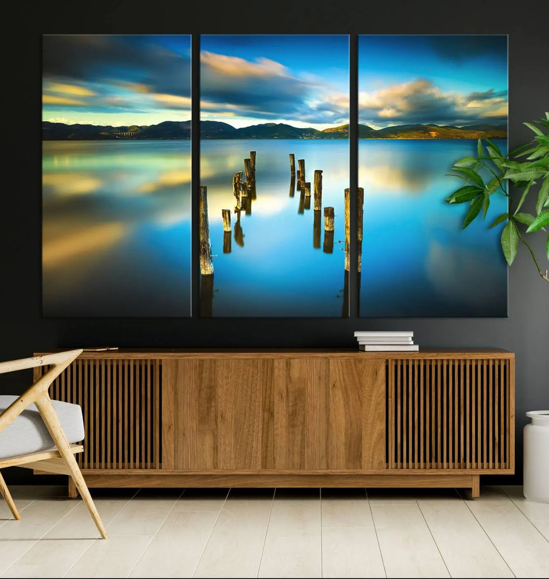 A triptych of a serene lake scene with old wooden pillars, blue sky, and clouds casts a coastal ambiance. The Sea Ocean Sunset Beach Wall Art Canvas Print reflects the soothing nature of the ocean.