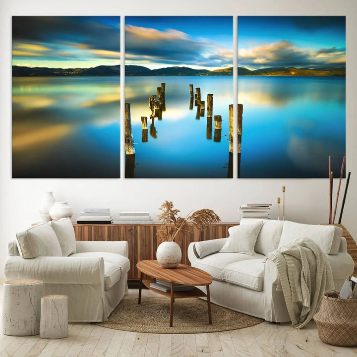 A triptych of a serene lake scene with old wooden pillars, blue sky, and clouds casts a coastal ambiance. The Sea Ocean Sunset Beach Wall Art Canvas Print reflects the soothing nature of the ocean.