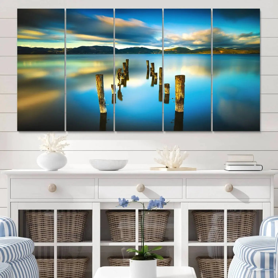 A triptych of a serene lake scene with old wooden pillars, blue sky, and clouds casts a coastal ambiance. The Sea Ocean Sunset Beach Wall Art Canvas Print reflects the soothing nature of the ocean.