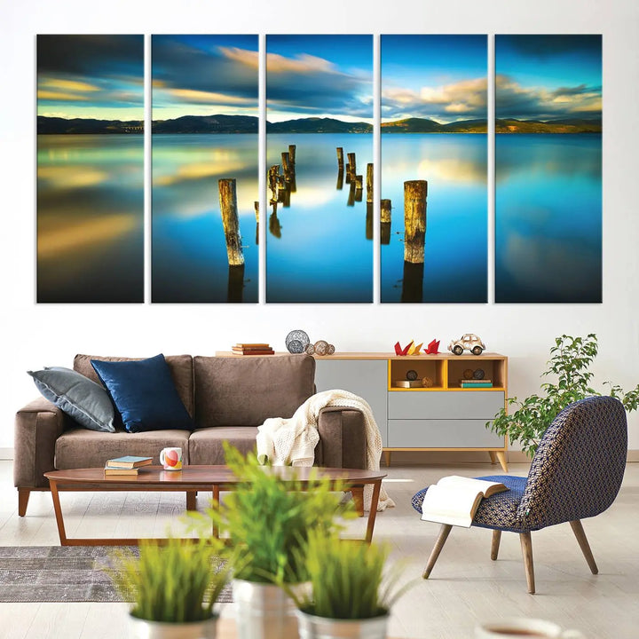 A triptych of a serene lake scene with old wooden pillars, blue sky, and clouds casts a coastal ambiance. The Sea Ocean Sunset Beach Wall Art Canvas Print reflects the soothing nature of the ocean.