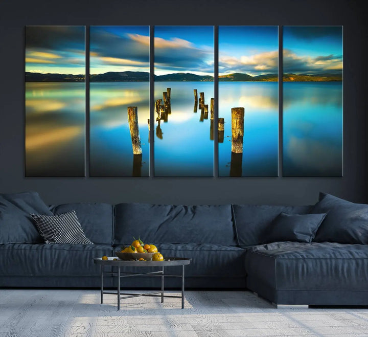 A triptych of a serene lake scene with old wooden pillars, blue sky, and clouds casts a coastal ambiance. The Sea Ocean Sunset Beach Wall Art Canvas Print reflects the soothing nature of the ocean.