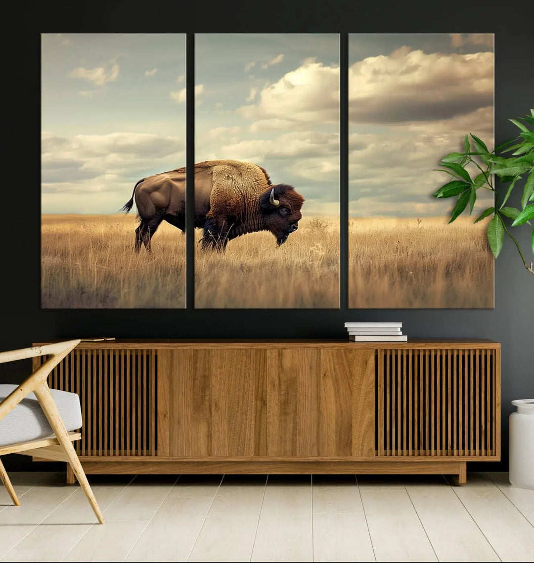 The Sepia American Bison Wall Art Print, a Western canvas print, depicts a bison standing in a grassy field beneath a cloudy sky. This high-resolution museum-quality triptych wall art is ideal for farmhouse wall decor.