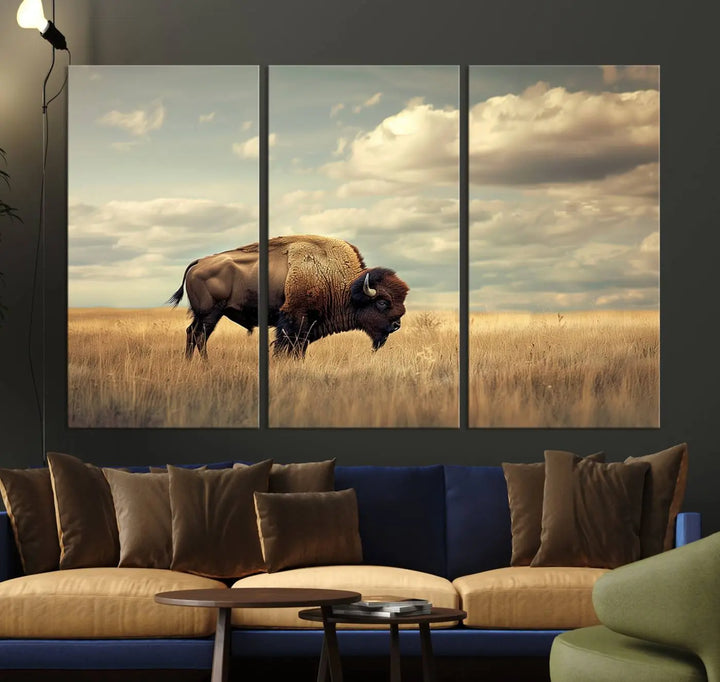 The Sepia American Bison Wall Art Print, a Western canvas print, depicts a bison standing in a grassy field beneath a cloudy sky. This high-resolution museum-quality triptych wall art is ideal for farmhouse wall decor.