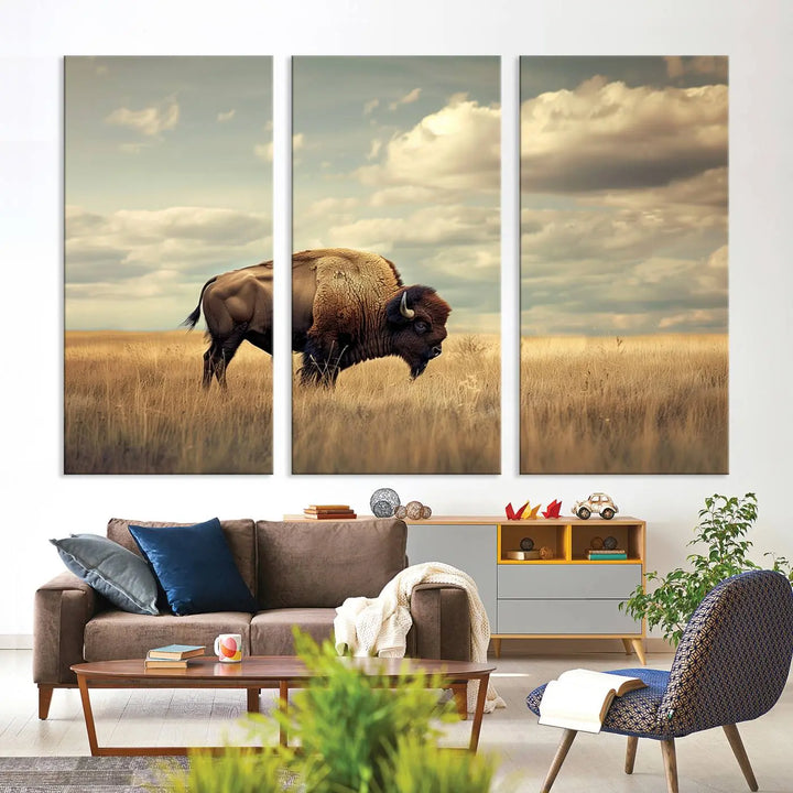 The Sepia American Bison Wall Art Print, a Western canvas print, depicts a bison standing in a grassy field beneath a cloudy sky. This high-resolution museum-quality triptych wall art is ideal for farmhouse wall decor.