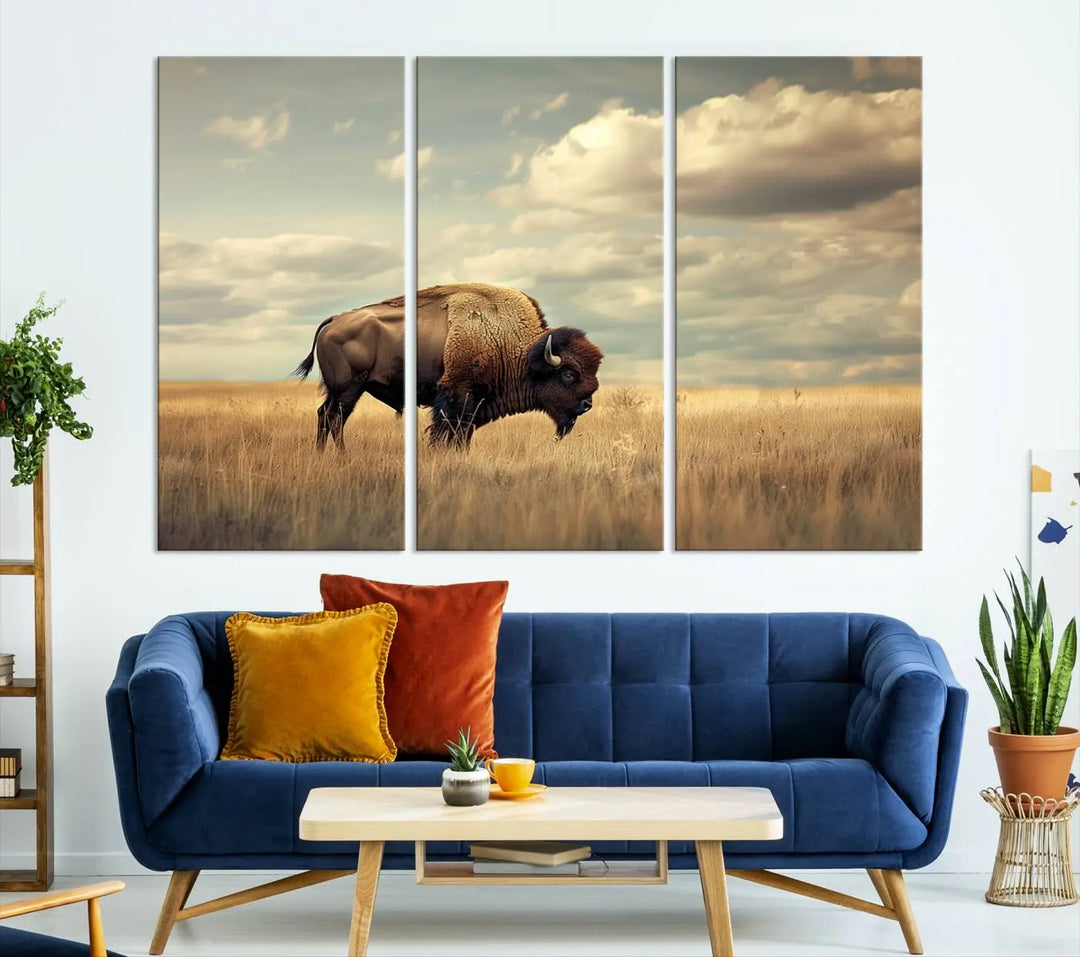 The Sepia American Bison Wall Art Print, a Western canvas print, depicts a bison standing in a grassy field beneath a cloudy sky. This high-resolution museum-quality triptych wall art is ideal for farmhouse wall decor.