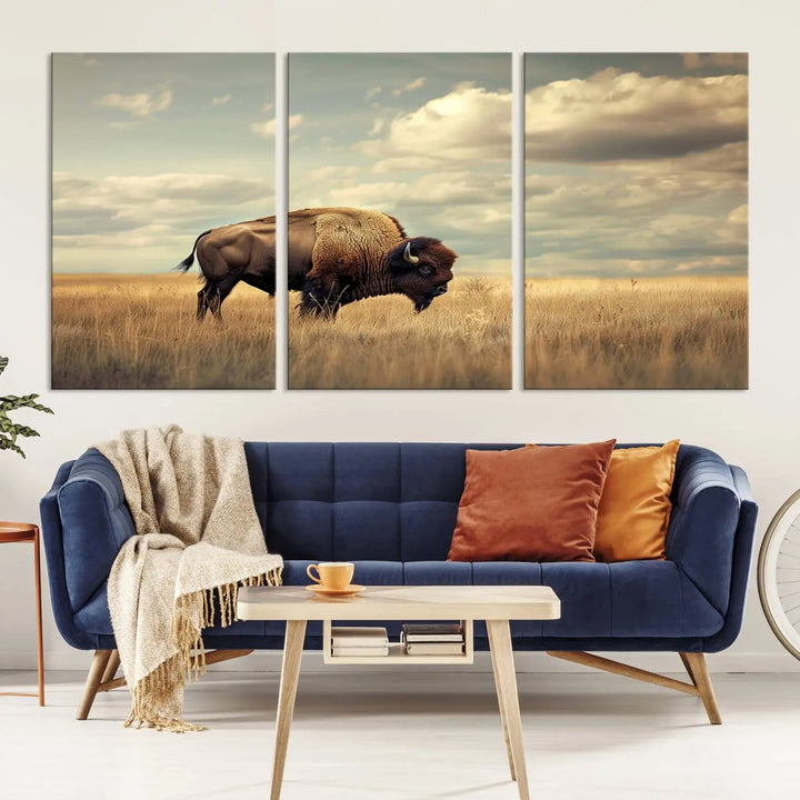 The Sepia American Bison Wall Art Print, a Western canvas print, depicts a bison standing in a grassy field beneath a cloudy sky. This high-resolution museum-quality triptych wall art is ideal for farmhouse wall decor.