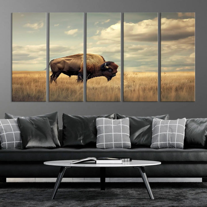 The Sepia American Bison Wall Art Print, a Western canvas print, depicts a bison standing in a grassy field beneath a cloudy sky. This high-resolution museum-quality triptych wall art is ideal for farmhouse wall decor.