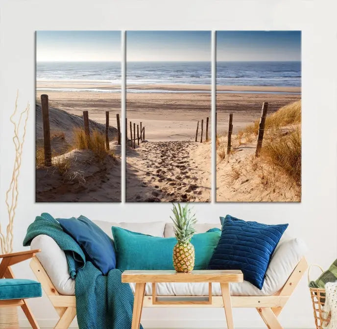 The "Serene Beach Path Canvas – Coastal Landscape Wall Art Triptych – Tranquil Ocean View for Living Room" is tastefully displayed, adding a beautiful coastal touch to the room's ambiance.