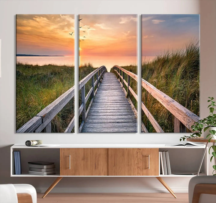 The Sunset Lakeside Pier Wall Art Canvas Print depicts a boardwalk leading towards a sunset over the ocean, framed by grassy dunes. Each piece is meticulously hand-assembled using museum-quality canvas to guarantee durability and vibrant colors.