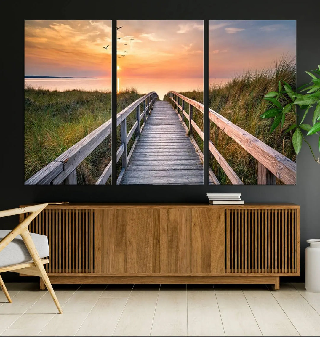 The Sunset Lakeside Pier Wall Art Canvas Print depicts a boardwalk leading towards a sunset over the ocean, framed by grassy dunes. Each piece is meticulously hand-assembled using museum-quality canvas to guarantee durability and vibrant colors.