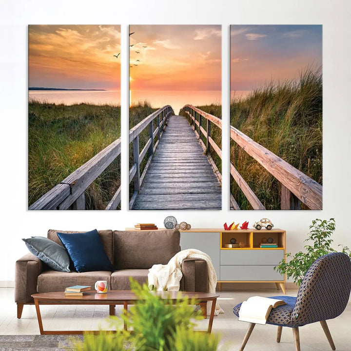 The Sunset Lakeside Pier Wall Art Canvas Print depicts a boardwalk leading towards a sunset over the ocean, framed by grassy dunes. Each piece is meticulously hand-assembled using museum-quality canvas to guarantee durability and vibrant colors.