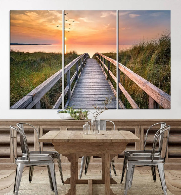 The Sunset Lakeside Pier Wall Art Canvas Print depicts a boardwalk leading towards a sunset over the ocean, framed by grassy dunes. Each piece is meticulously hand-assembled using museum-quality canvas to guarantee durability and vibrant colors.