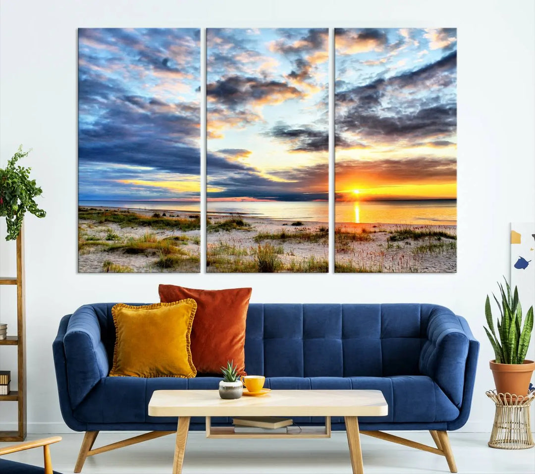 The living room features the Sunset On The Ocean Wall Art Canvas Print, a stunning large triptych depicting a sunset over a beach. This artwork is elegantly displayed on museum-quality canvas with UV-protective coating, ensuring both beauty and durability.