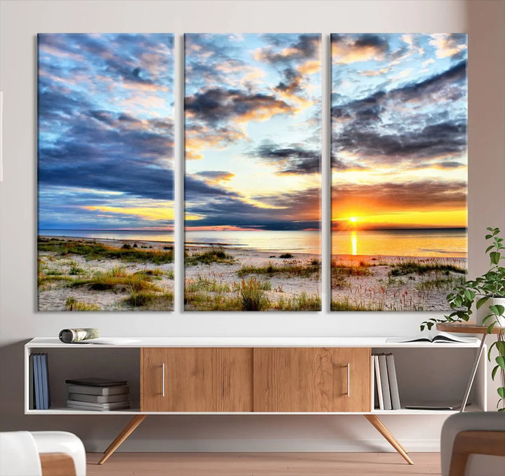 The living room features the Sunset On The Ocean Wall Art Canvas Print, a stunning large triptych depicting a sunset over a beach. This artwork is elegantly displayed on museum-quality canvas with UV-protective coating, ensuring both beauty and durability.