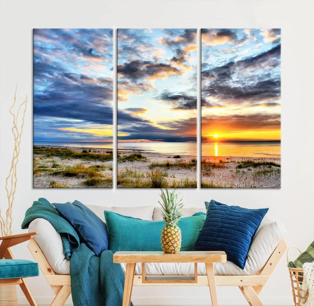 The living room features the Sunset On The Ocean Wall Art Canvas Print, a stunning large triptych depicting a sunset over a beach. This artwork is elegantly displayed on museum-quality canvas with UV-protective coating, ensuring both beauty and durability.