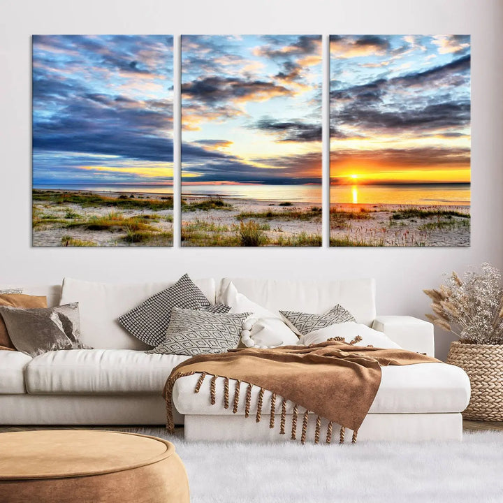 The living room features the Sunset On The Ocean Wall Art Canvas Print, a stunning large triptych depicting a sunset over a beach. This artwork is elegantly displayed on museum-quality canvas with UV-protective coating, ensuring both beauty and durability.