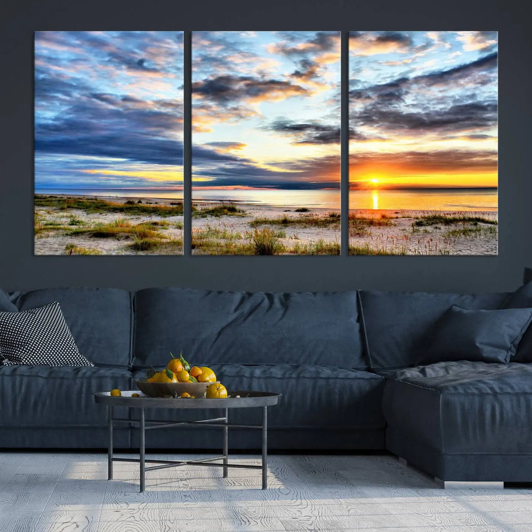 The living room features the Sunset On The Ocean Wall Art Canvas Print, a stunning large triptych depicting a sunset over a beach. This artwork is elegantly displayed on museum-quality canvas with UV-protective coating, ensuring both beauty and durability.