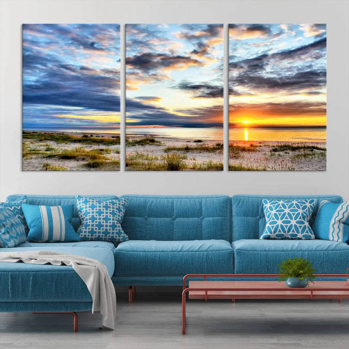 The living room features the Sunset On The Ocean Wall Art Canvas Print, a stunning large triptych depicting a sunset over a beach. This artwork is elegantly displayed on museum-quality canvas with UV-protective coating, ensuring both beauty and durability.