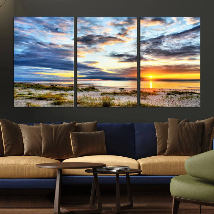 The living room features the Sunset On The Ocean Wall Art Canvas Print, a stunning large triptych depicting a sunset over a beach. This artwork is elegantly displayed on museum-quality canvas with UV-protective coating, ensuring both beauty and durability.