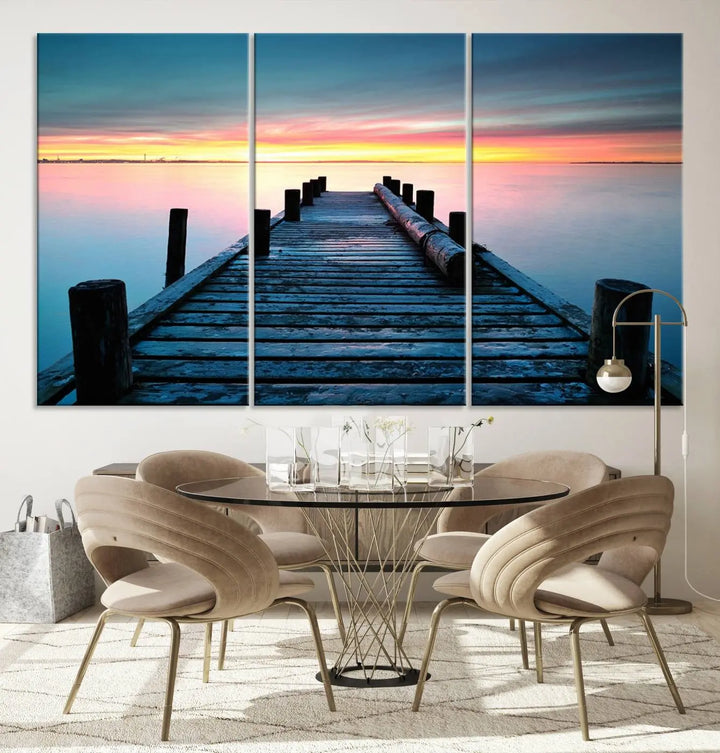 The "Sunset Pier Triptych Canvas Art," a giclee print known for its Canon print quality and gallery wrap finish, captures a wooden pier stretching into a tranquil lake at sunset beneath vibrant orange and blue skies. It makes an ideal centerpiece for coastal-themed art settings.