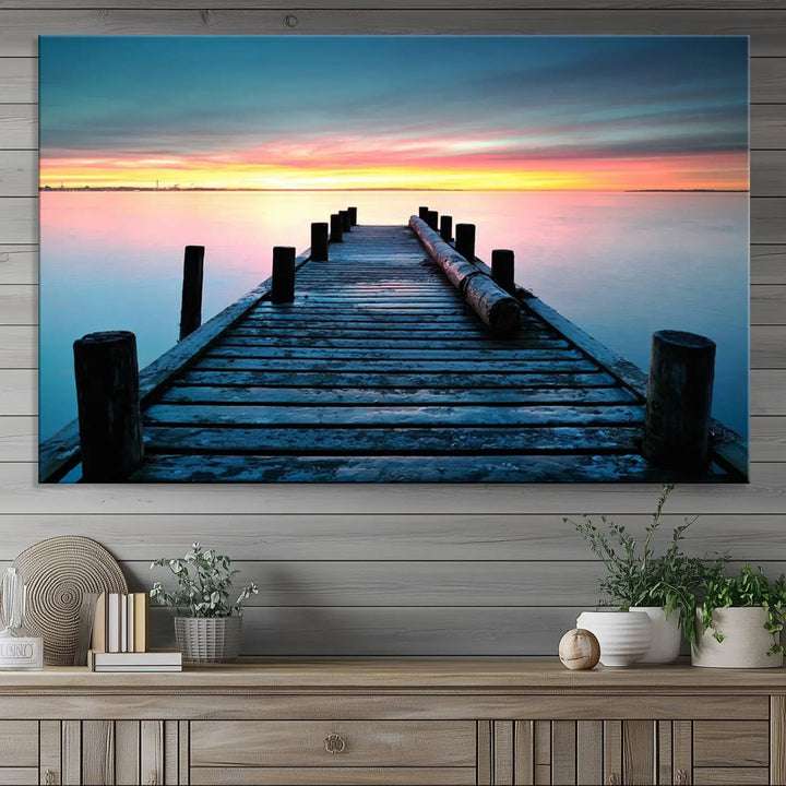 The "Sunset Pier Triptych Canvas Art," a giclee print known for its Canon print quality and gallery wrap finish, captures a wooden pier stretching into a tranquil lake at sunset beneath vibrant orange and blue skies. It makes an ideal centerpiece for coastal-themed art settings.