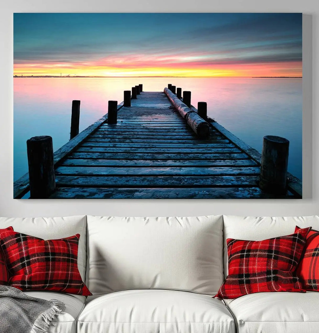 The "Sunset Pier Triptych Canvas Art," a giclee print known for its Canon print quality and gallery wrap finish, captures a wooden pier stretching into a tranquil lake at sunset beneath vibrant orange and blue skies. It makes an ideal centerpiece for coastal-themed art settings.