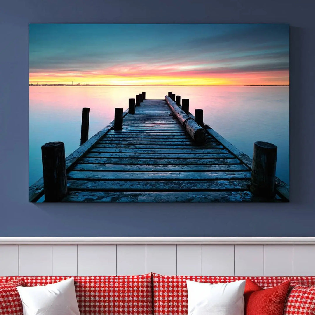 The "Sunset Pier Triptych Canvas Art," a giclee print known for its Canon print quality and gallery wrap finish, captures a wooden pier stretching into a tranquil lake at sunset beneath vibrant orange and blue skies. It makes an ideal centerpiece for coastal-themed art settings.