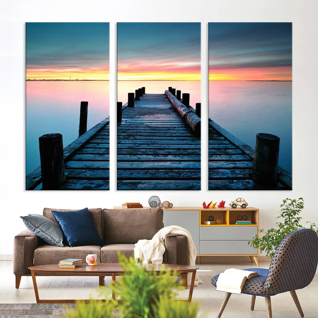 The "Sunset Pier Triptych Canvas Art," a giclee print known for its Canon print quality and gallery wrap finish, captures a wooden pier stretching into a tranquil lake at sunset beneath vibrant orange and blue skies. It makes an ideal centerpiece for coastal-themed art settings.