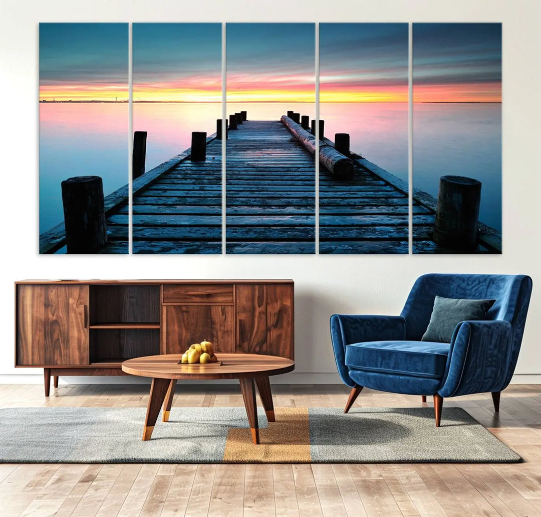 The "Sunset Pier Triptych Canvas Art," a giclee print known for its Canon print quality and gallery wrap finish, captures a wooden pier stretching into a tranquil lake at sunset beneath vibrant orange and blue skies. It makes an ideal centerpiece for coastal-themed art settings.