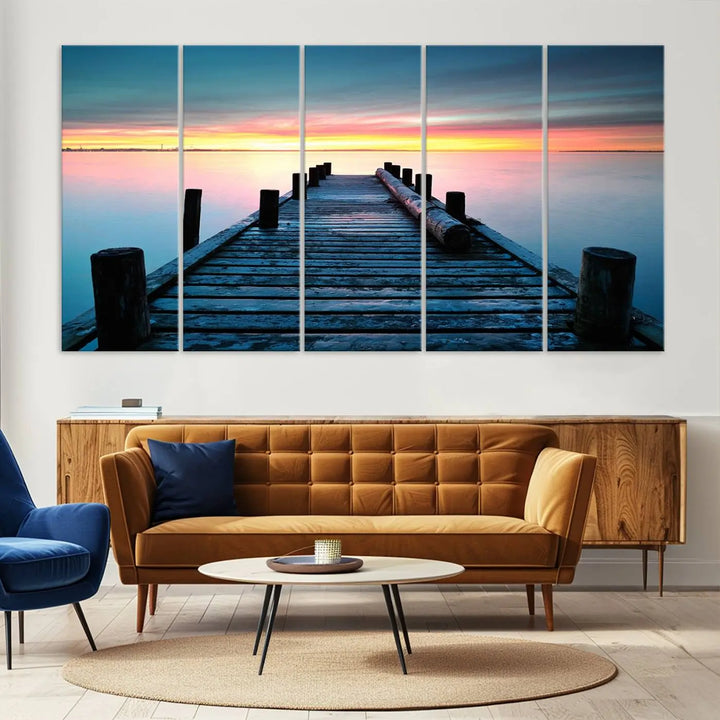 The "Sunset Pier Triptych Canvas Art," a giclee print known for its Canon print quality and gallery wrap finish, captures a wooden pier stretching into a tranquil lake at sunset beneath vibrant orange and blue skies. It makes an ideal centerpiece for coastal-themed art settings.