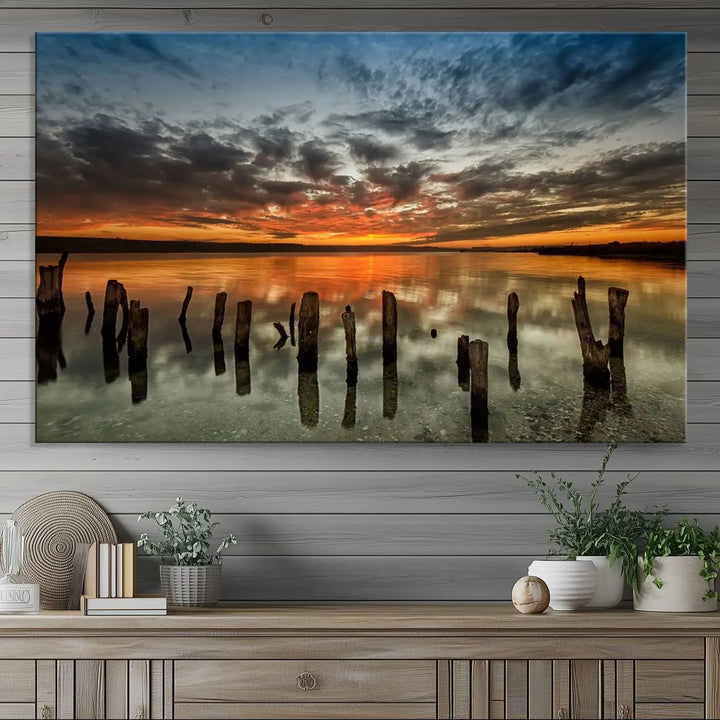 The "Sunset Reflection on Wooden Pier Giclee Canvas Print" is a panoramic wall art piece showcasing serene nature photography with a colorful sunset over water and wooden posts.