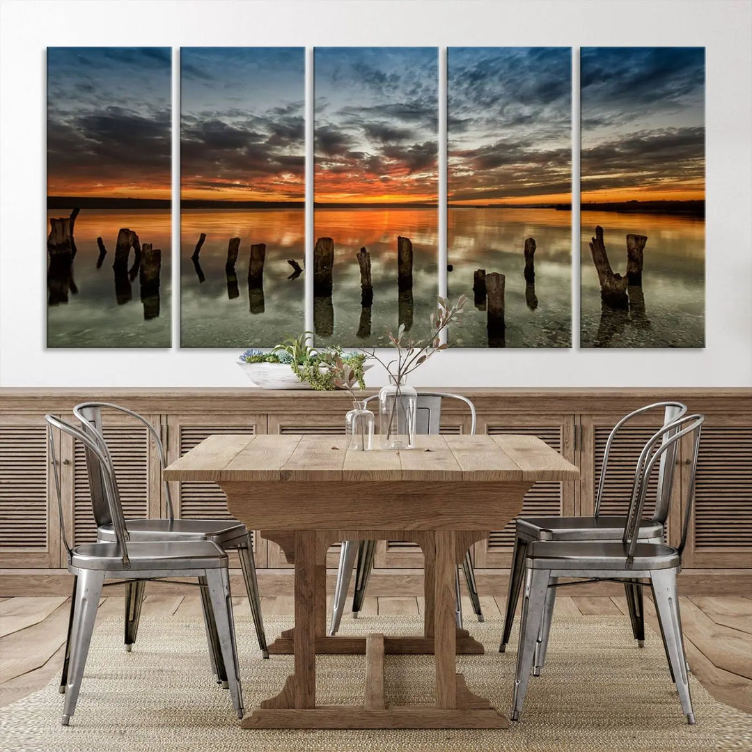 The "Sunset Reflection on Wooden Pier Giclee Canvas Print" is a panoramic wall art piece showcasing serene nature photography with a colorful sunset over water and wooden posts.