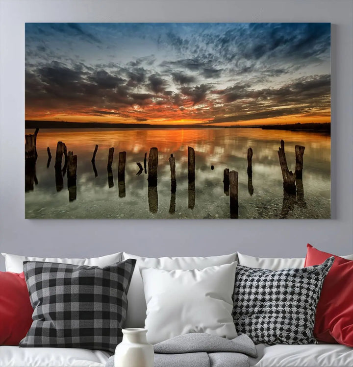 The "Sunset Reflection on Wooden Pier Giclee Canvas Print" is a panoramic wall art piece showcasing serene nature photography with a colorful sunset over water and wooden posts.