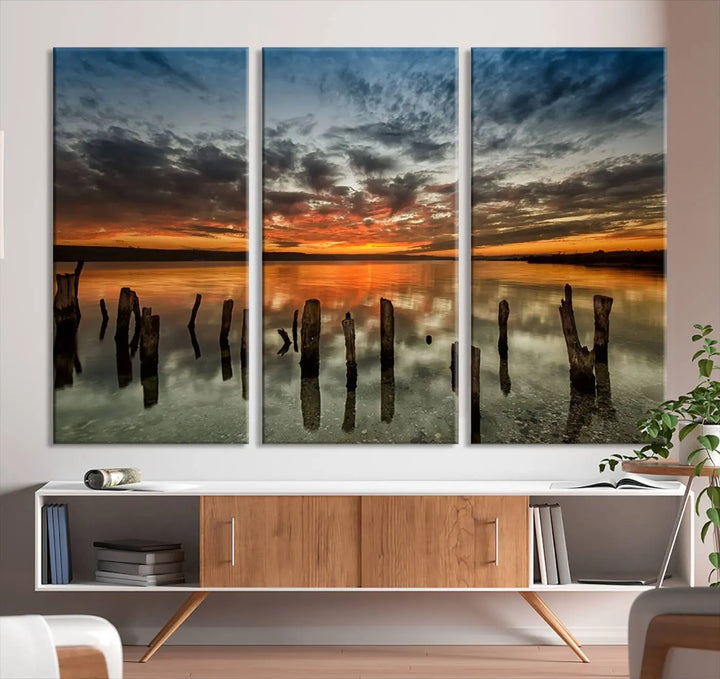 The "Sunset Reflection on Wooden Pier Giclee Canvas Print" is a panoramic wall art piece showcasing serene nature photography with a colorful sunset over water and wooden posts.