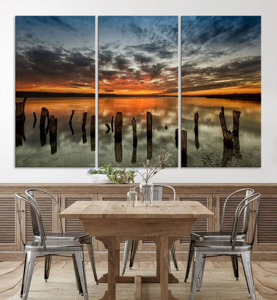 The "Sunset Reflection on Wooden Pier Giclee Canvas Print" is a panoramic wall art piece showcasing serene nature photography with a colorful sunset over water and wooden posts.