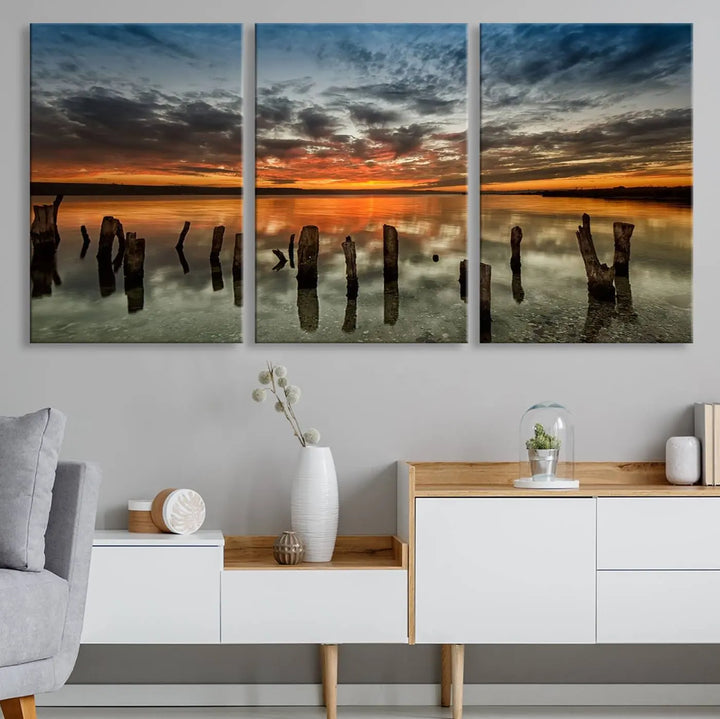 The "Sunset Reflection on Wooden Pier Giclee Canvas Print" is a panoramic wall art piece showcasing serene nature photography with a colorful sunset over water and wooden posts.