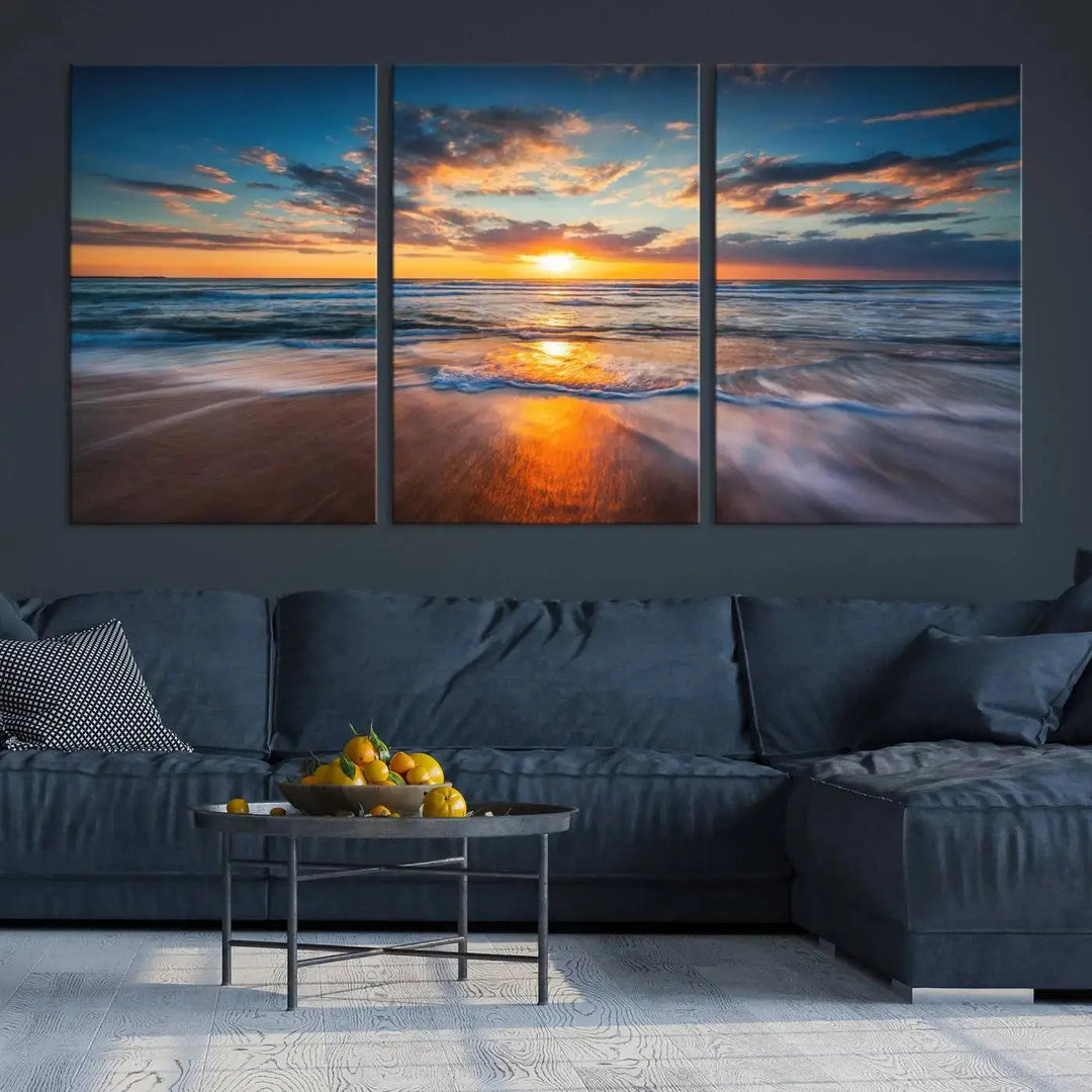 The Sunset on Beach Canvas Wall Art Canvas Print is a triptych depicting a sunset over the ocean. Each piece of this museum-quality polycotton canvas is gallery wrapped and has a UV-protective coating to maintain its vibrant colors. It is displayed on a living room wall.