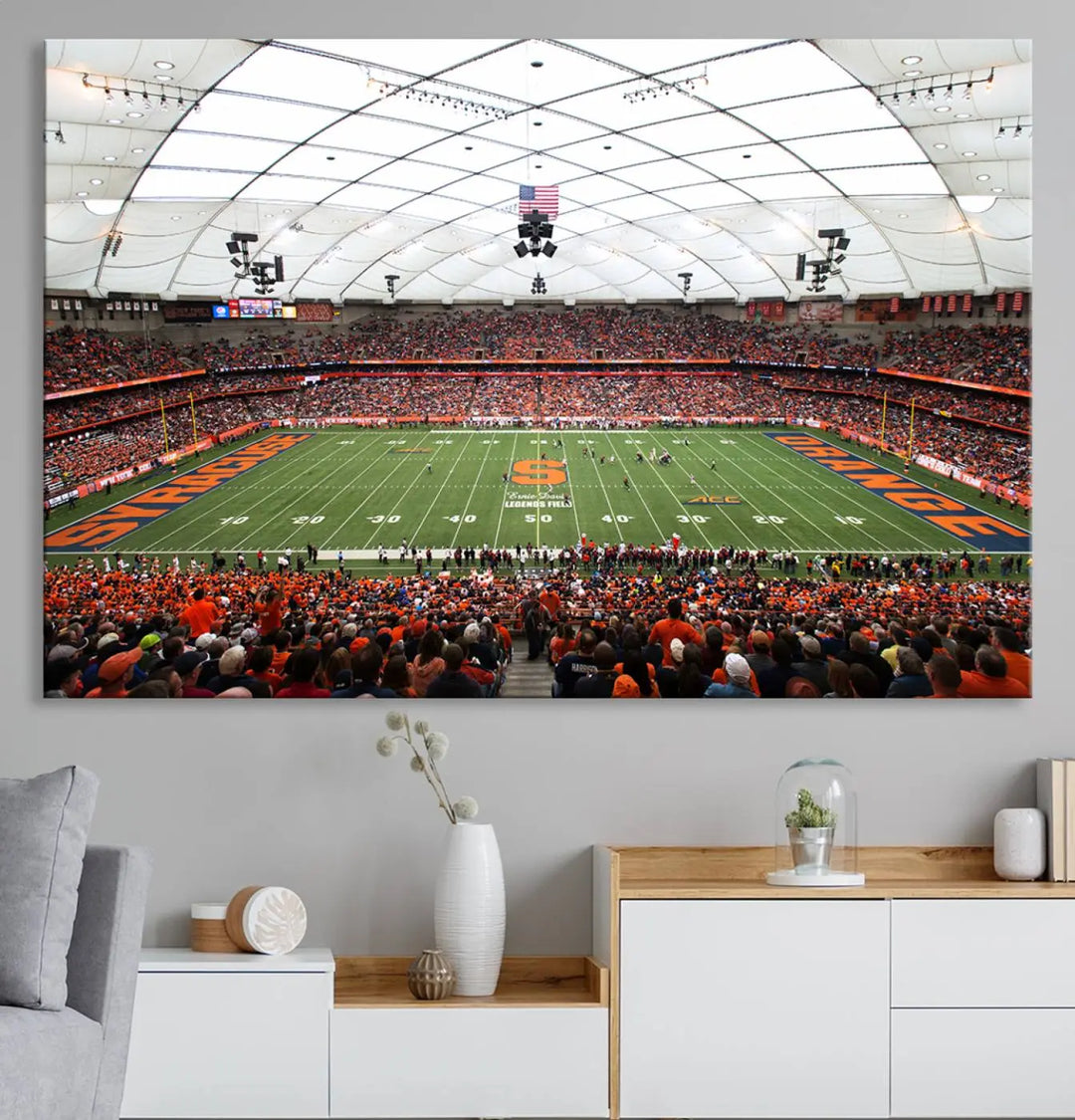 The living room boasts a sizable, three-panel canvas artwork on the wall, depicting the vibrant crowd of the Syracuse University Orange football team at Syracuse JMA Wireless Dome, complete with a gallery-quality finish.