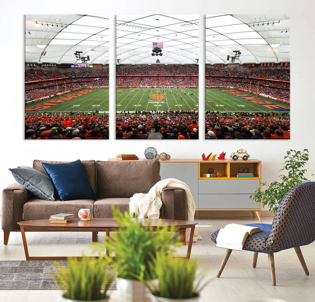 The living room boasts a sizable, three-panel canvas artwork on the wall, depicting the vibrant crowd of the Syracuse University Orange football team at Syracuse JMA Wireless Dome, complete with a gallery-quality finish.