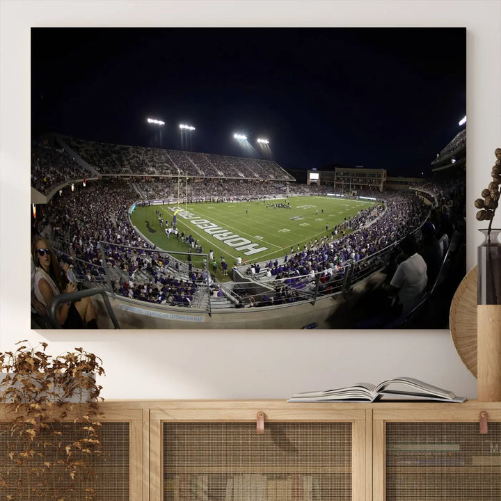 Immerse yourself in the vibrant energy of a packed football stadium at night with bright lights illuminating the field and stands, beautifully captured in the TCU Horned Frogs Football Team Print on premium canvas. This wall art features Fort Worth's Amon G. Carter Stadium.