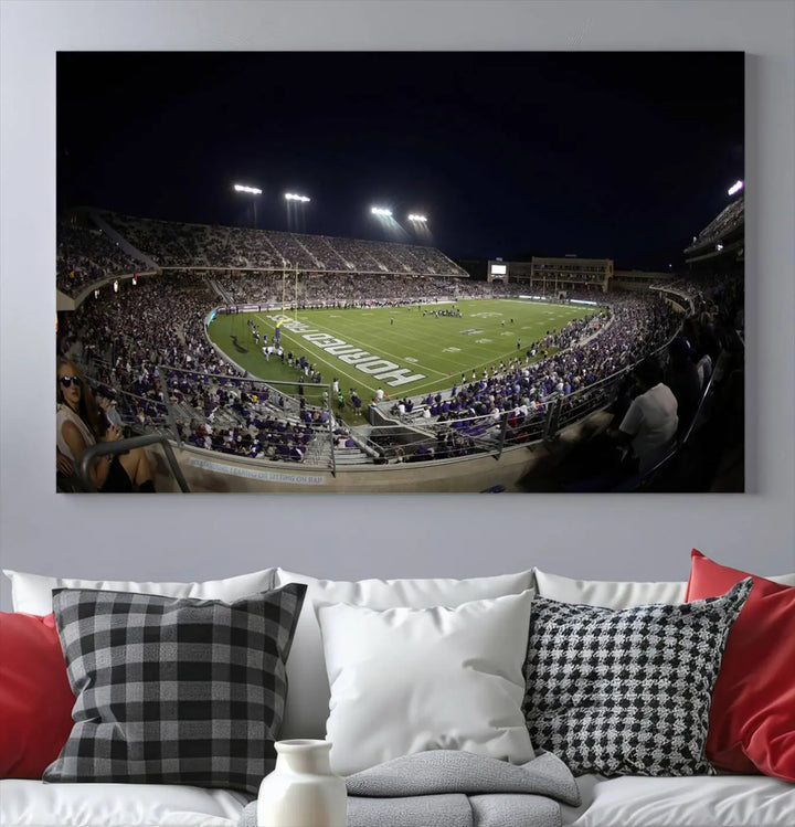 Immerse yourself in the vibrant energy of a packed football stadium at night with bright lights illuminating the field and stands, beautifully captured in the TCU Horned Frogs Football Team Print on premium canvas. This wall art features Fort Worth's Amon G. Carter Stadium.