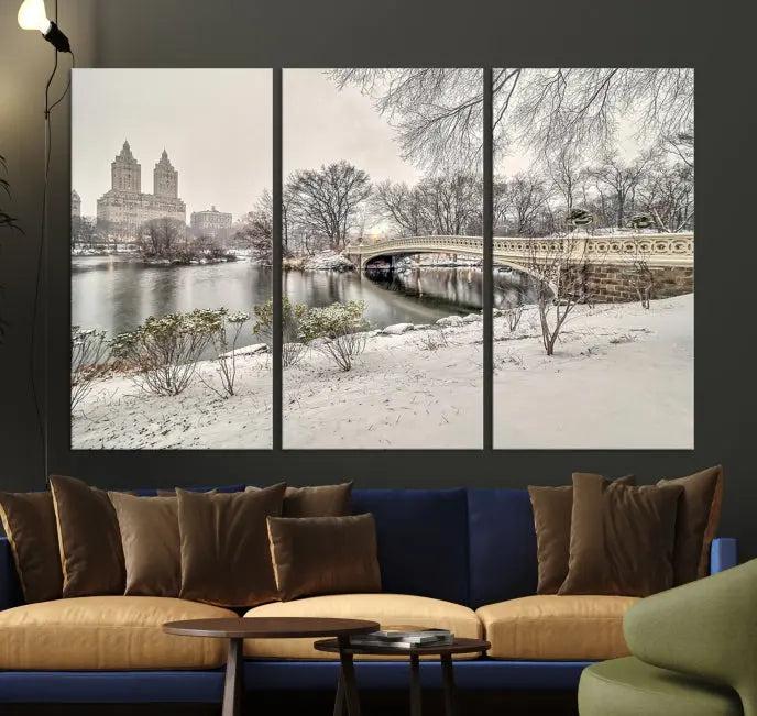 The Bow Bridge in Central Park Canvas Print features a snowy scene with a bridge and city buildings in the background. This museum-quality canvas comes with a UV-protective coating and is ready to hang.