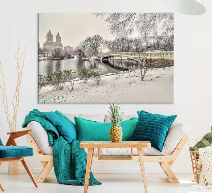 The Bow Bridge in Central Park Canvas Print features a snowy scene with a bridge and city buildings in the background. This museum-quality canvas comes with a UV-protective coating and is ready to hang.