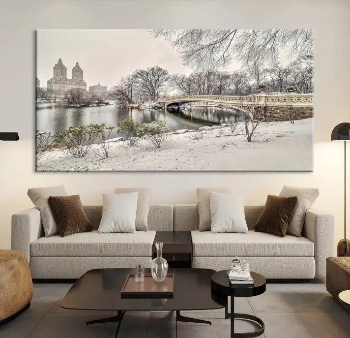 The Bow Bridge in Central Park Canvas Print features a snowy scene with a bridge and city buildings in the background. This museum-quality canvas comes with a UV-protective coating and is ready to hang.