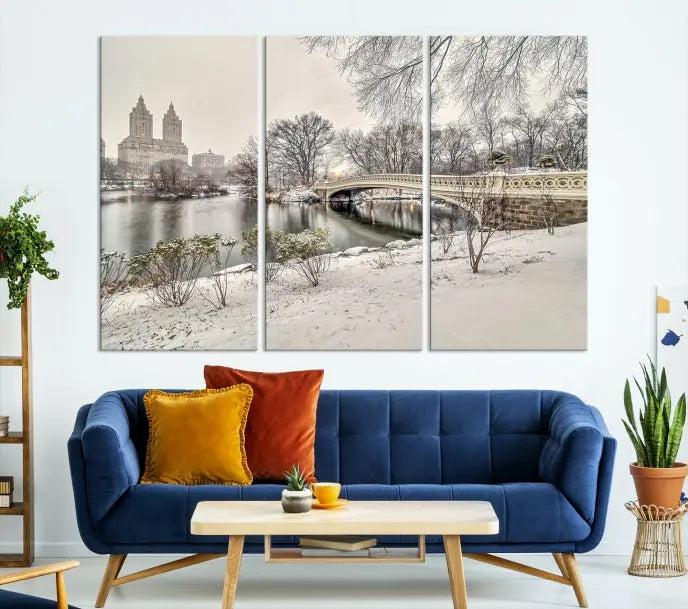 The Bow Bridge in Central Park Canvas Print features a snowy scene with a bridge and city buildings in the background. This museum-quality canvas comes with a UV-protective coating and is ready to hang.