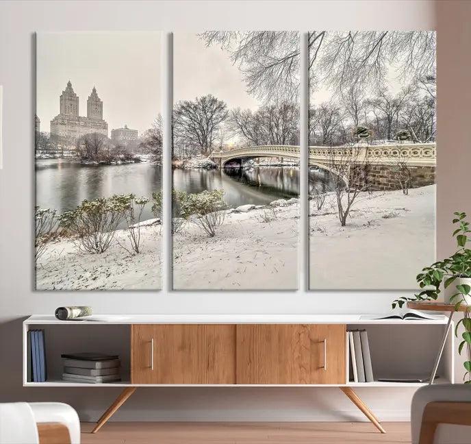 The Bow Bridge in Central Park Canvas Print features a snowy scene with a bridge and city buildings in the background. This museum-quality canvas comes with a UV-protective coating and is ready to hang.