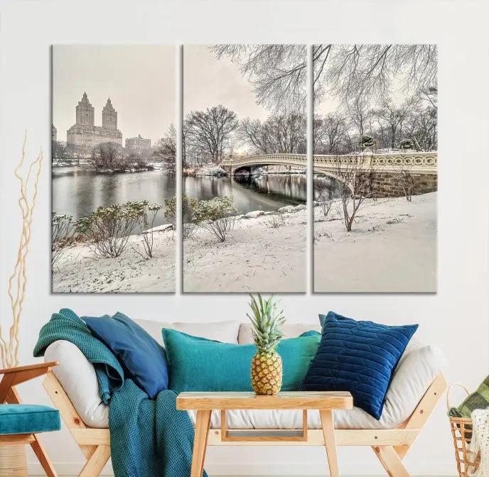 The Bow Bridge in Central Park Canvas Print features a snowy scene with a bridge and city buildings in the background. This museum-quality canvas comes with a UV-protective coating and is ready to hang.