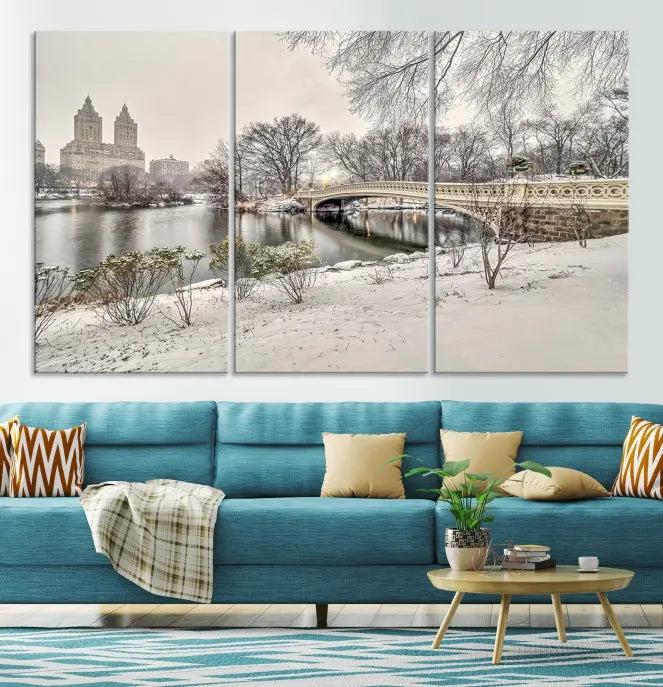 The Bow Bridge in Central Park Canvas Print features a snowy scene with a bridge and city buildings in the background. This museum-quality canvas comes with a UV-protective coating and is ready to hang.